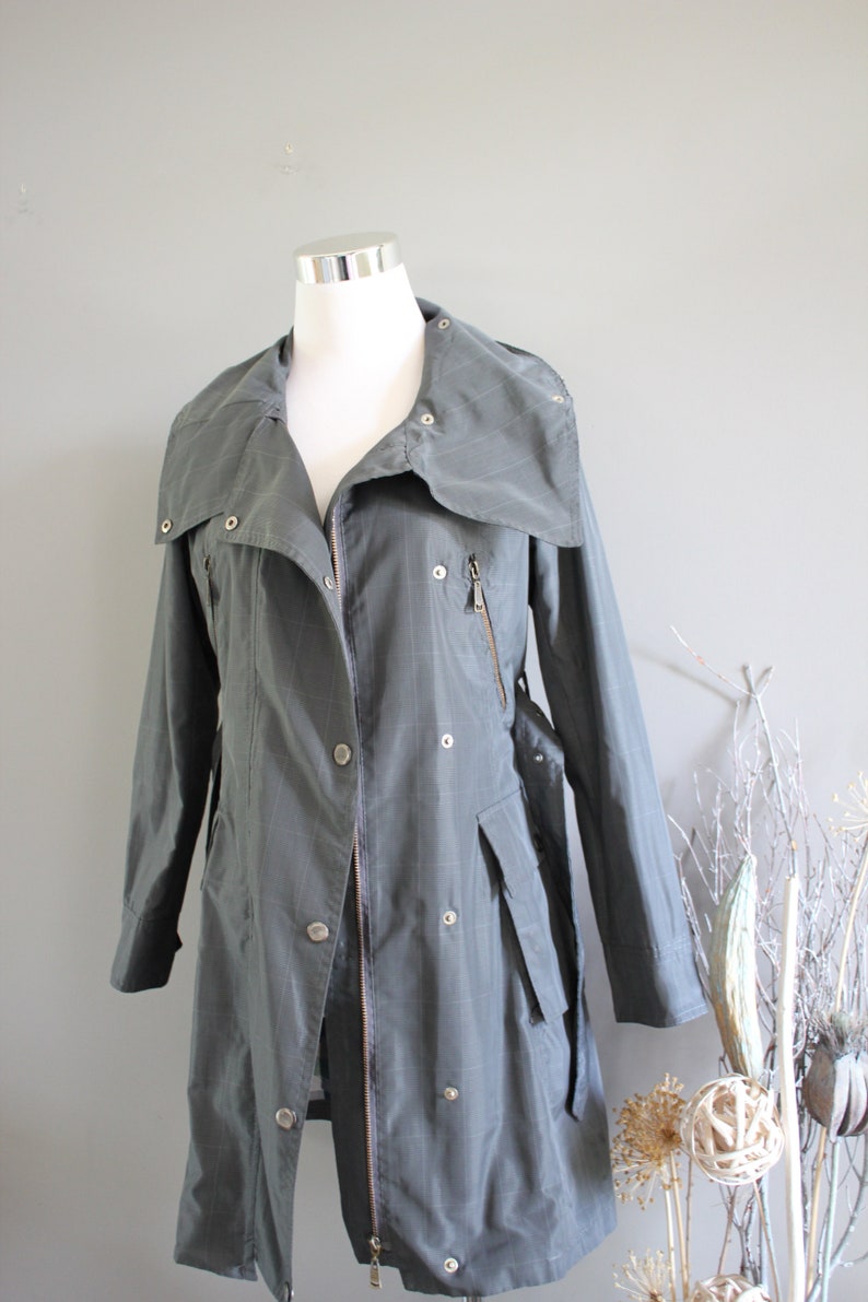 May include: A long, gray, collared jacket with a zipper and buttons. The jacket has a belt and pockets.