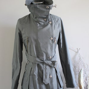 May include: A gray, belted trench coat with a high collar and a button closure. The coat has a pinstripe pattern and a zippered pocket on the left side.