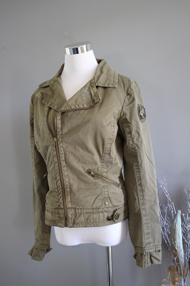 May include: A green, zippered, moto-style jacket with a decorative patch on the sleeve.