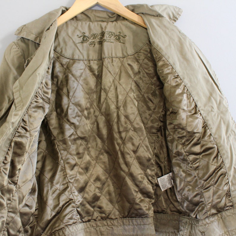 May include: A green quilted jacket with a brown lining. The jacket has a zipper closure and a collar. The inside of the jacket has a label with the text "Sweet" and a floral design.