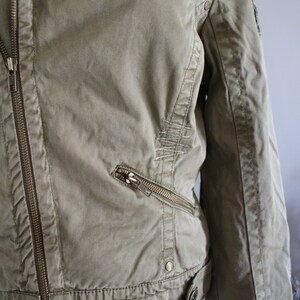 May include: A green canvas jacket with a zipper closure and multiple pockets. The jacket has a distressed look with stitching details.