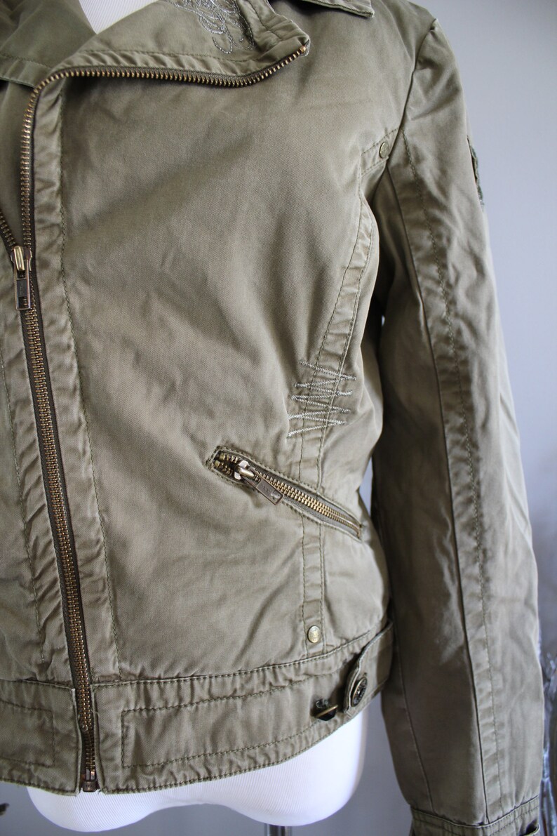 May include: A green canvas jacket with a zipper closure and multiple pockets. The jacket has a distressed look with stitching details.