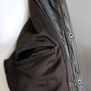 K&ouml;nnte beinhalten: Nahaufnahme des Innenfutters einer braunen Lederjacke, die ein schwarzes Stofffutter und eine Rei&szlig;verschlusstasche zeigt.