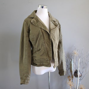 May include: A green, zippered, collared jacket with a slightly asymmetrical zipper closure. The jacket has a slim fit and is made of a soft, textured fabric.