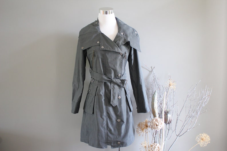 May include: A long-sleeved, olive green, belted trench coat with a zipper and button closure. The coat has a collar that can be worn up or down.