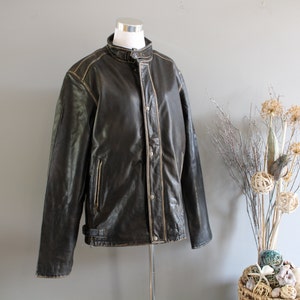 K&ouml;nnte beinhalten: Eine braune Lederjacke mit Stehkragen und Rei&szlig;verschluss. Die Jacke hat einen Used-Look und wei&szlig;e N&auml;hte.