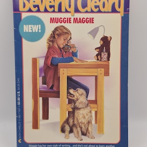 May include: A paperback book titled Muggie Maggie by Beverly Cleary. The cover features an illustration of a child sitting at a wooden desk writing, with a brown teddy bear, a desk lamp, and a light brown dog sitting on the floor nearby.