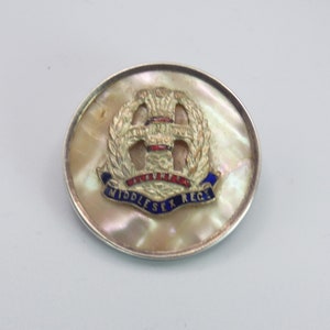 May include: A silver and mother-of-pearl brooch featuring a gold and enamel Middlesex Regiment crest.