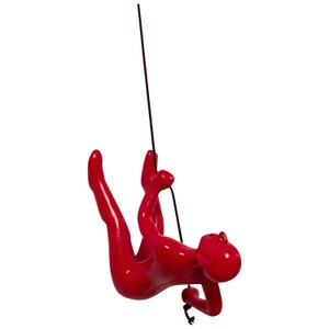 May include: A glossy red figurine of a person climbing a black rope. The figure is in a dynamic pose, with arms and legs extended as if ascending or descending. The figurine is a solid color with a smooth finish.