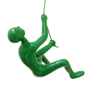 May include: A green figurine of a person rappelling down a rope. The figurine is made of a smooth, glossy material and has a realistic design.