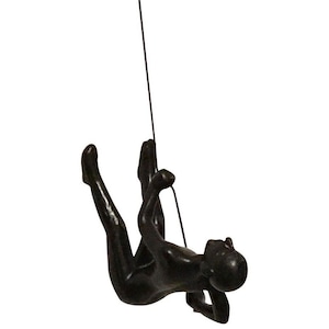 May include: A black metal sculpture of a person rappelling down a rope. The sculpture is suspended in mid-air and appears to be in motion.