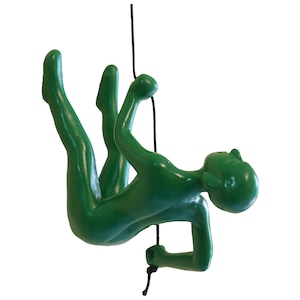May include: Green figurine of a person hanging from a rope, with one hand holding the rope and the other reaching out. The figurine is in a dynamic pose, suggesting movement and action.