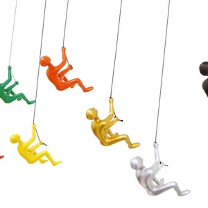 May include: Seven colorful hanging figurines of people rock climbing, with a black figurine in the background.