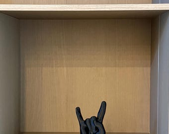 May include: A black sculpture of a hand making the rock and roll hand gesture, placed on a shelf inside a wooden cabinet. The cabinet has three shelves and a light wood grain finish.
