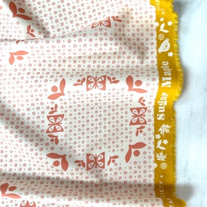 May include: Cream-coloured fabric featuring a repeating pattern of small brown flowers and larger brown butterfly and leaf designs. A yellow border with the text "Sugar Maple" and floral illustrations runs along the edge.
