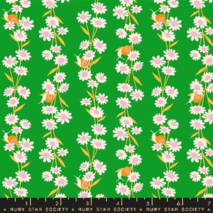 May include: A green fabric with a repeating pattern of white flowers and orange snails. The fabric has a white ruler with black markings at the bottom.