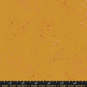 May include: A mustard yellow fabric with a speckled pattern of pink and red dots. The fabric is a cotton blend and is perfect for quilting, sewing, and crafting.