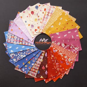 Peut inclure: Un arrangement circulaire d'échantillons de tissu dans un spectre de couleurs incluant crème, jaune, rose, rouge, bleu et marron. Chaque échantillon présente des motifs distincts comme des fleurs, des formes géométriques et des icônes. Une étiquette centrale indique PERSIMMON.