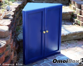 Può includere: Un armadio d'angolo blu con due ante e pomelli dorati. L'armadio è posizionato su un patio in mattoni.