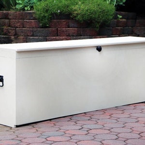 May include: A white storage box with a hinged lid and a black handle. The box is sitting on a brick patio.