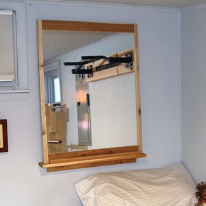 Op de afbeelding: Een slaapkamer met een houten pull-up bar aan de muur, een spiegel en een bed met een wit kussen en een knuffel. De muur heeft de tekst "Positive Thinking" erop.