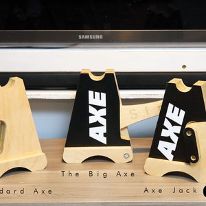 Puede incluir: Tres soportes de entrenamiento de madera, etiquetados como "Standard Axe", "The Big Axe" y "Axe Jack". Los soportes están hechos de madera natural y tienen una superficie pintada de negro con letras blancas que dicen "AXE". Los soportes están diseñados para usarse con un hacha.