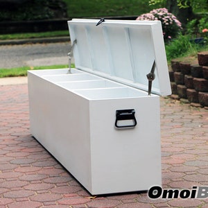 May include: White storage bench with three compartments and a hinged lid. The bench is made of wood and has a black handle. The bench is sitting on a brick patio.
