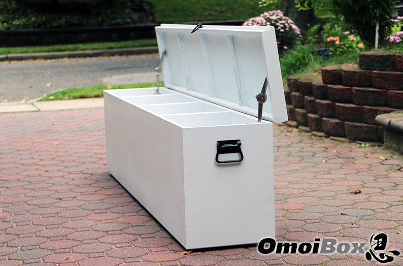 May include: White storage bench with three compartments and a hinged lid. The bench is made of wood and has a black handle. The bench is sitting on a brick patio.