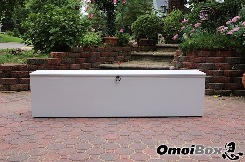 May include: White storage bench with a hinged lid and a black metal ring handle. The bench is sitting on a brick patio.
