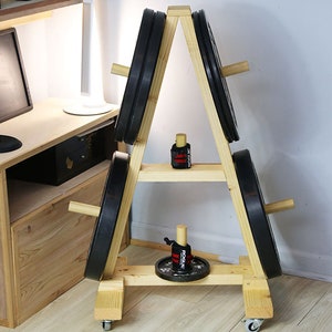 May include: A wooden weight plate stand with four weight plates and two pairs of wrist wraps. The stand has a triangular shape and is on wheels. The stand is made of light wood and has a natural finish.