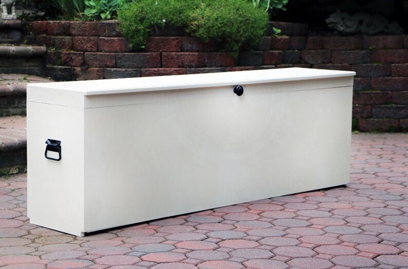 May include: A white storage box with a hinged lid and a black handle. The box is sitting on a brick patio.