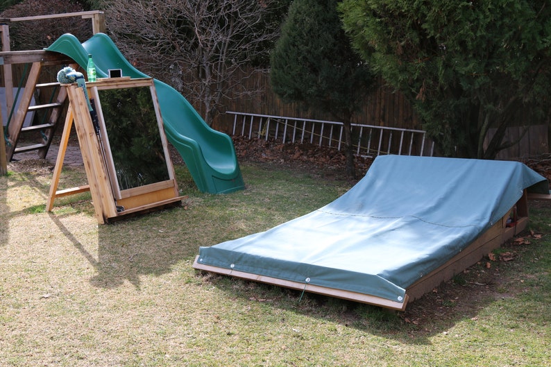 Puede incluir: Un tobog&aacute;n de pl&aacute;stico verde y un arenero de madera con una lona azul en un patio trasero.