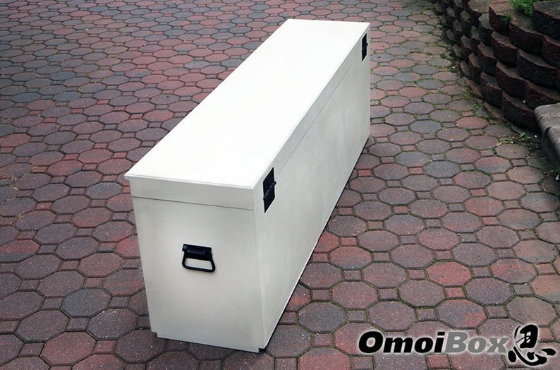 May include: A white wooden storage chest with two black metal handles and two black metal latches. The chest is sitting on a red brick patio.