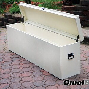 May include: A white storage bench with a hinged lid and a black handle. The bench is open and the inside is empty. The bench is sitting on a brick patio.