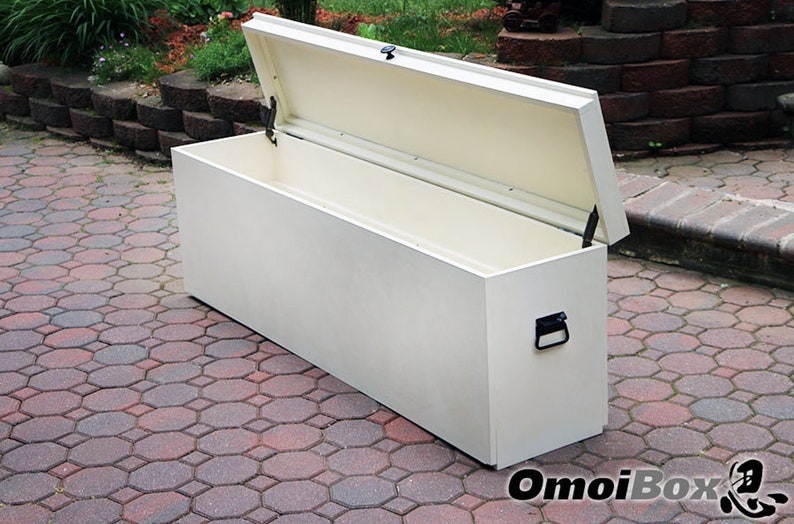 May include: A white storage bench with a hinged lid and a black handle. The bench is open and the inside is empty. The bench is sitting on a brick patio.