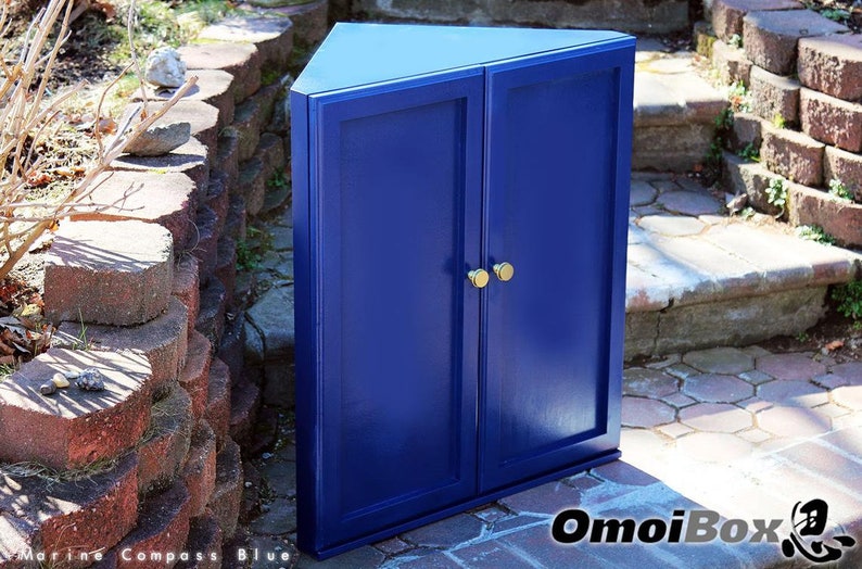 May include: A blue corner cabinet with two doors and gold knobs. The cabinet is sitting on a brick patio.