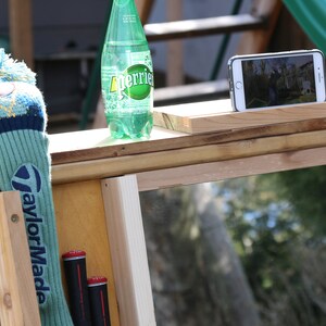 Puede incluir: Una estaci&oacute;n de pr&aacute;ctica de golf de madera con un espejo, una funda para la cabeza de un palo de golf, dos palos de golf y una botella de agua con gas Perrier. La estaci&oacute;n tiene un soporte para tel&eacute;fono en la parte superior.