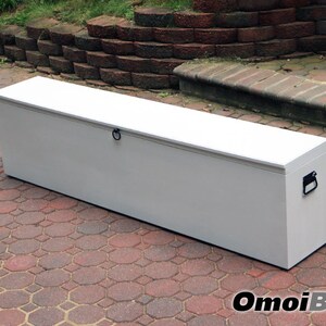 May include: A white storage chest with a hinged lid and two black handles. The chest is sitting on a red brick patio.