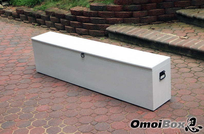 May include: A white storage chest with a hinged lid and two black handles. The chest is sitting on a red brick patio.