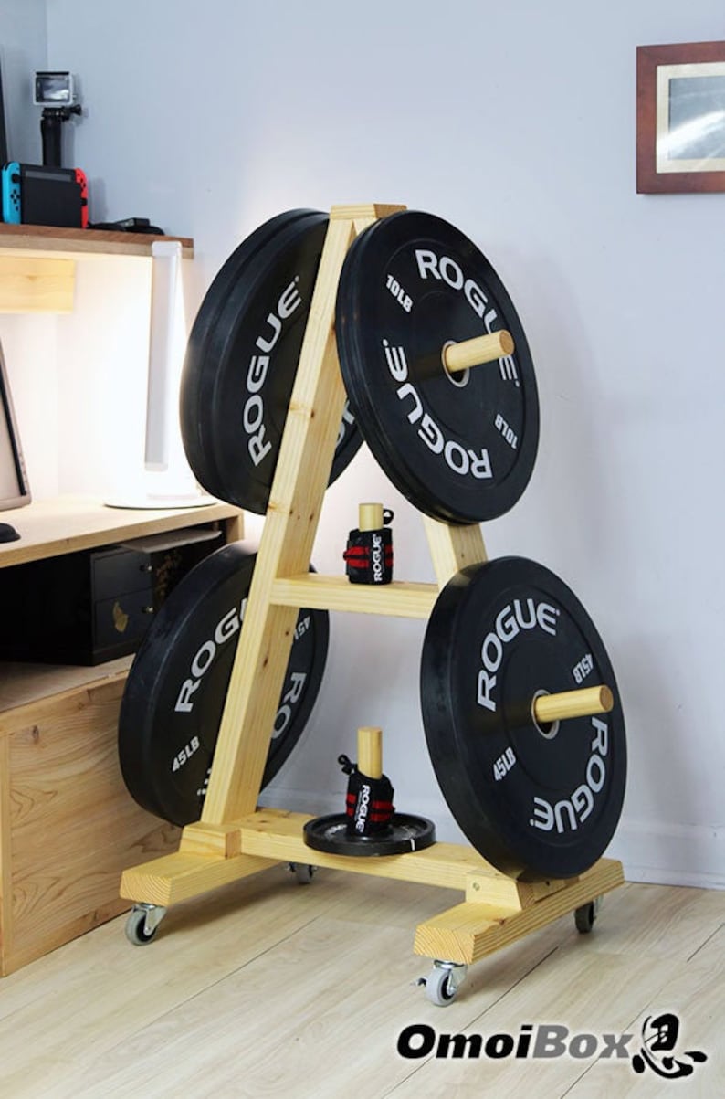 May include: A wooden weight plate storage rack with four black weight plates, each with the word "ROGUE" printed on them. The rack has four wheels and is made of natural wood.