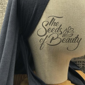 May include: A dark blue jersey knit fabric head wrap with a knotted tie. The fabric is draped over a mannequin head. The text "The Seeds of Beauty" is printed on the mannequin's chest.