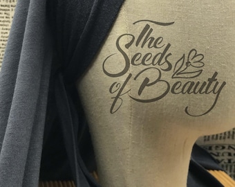 May include: A dark blue jersey knit fabric head wrap with a knotted tie. The fabric is draped over a mannequin head. The text "The Seeds of Beauty" is printed on the mannequin's chest.