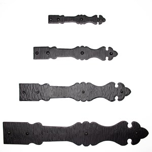 May include: Four black metal hinges of varying sizes. The hinges have a decorative, ornate design with a pointed tip. The hinges are arranged in a vertical row from smallest to largest.