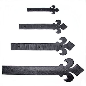 May include: Four black metal hinges with a fleur-de-lis design. The hinges are of varying sizes, with the largest hinge at the bottom and the smallest hinge at the top.