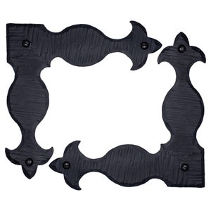 Puede incluir: Cuatro soportes de esquina de metal negro con un diseño decorativo. Cada soporte tiene una punta puntiaguda y una forma curva.