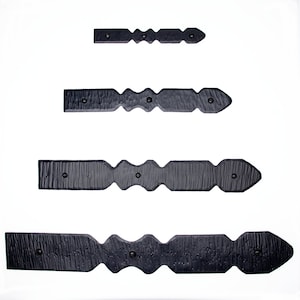 May include: Four black metal decorative hinges with a hammered finish and pointed ends. The hinges are arranged in a vertical row, with the largest hinge at the bottom and the smallest hinge at the top.