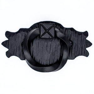 Puede incluir: Tirador de puerta de metal negro con un asa de anillo y una placa cuadrada decorativa con un diseño en X.