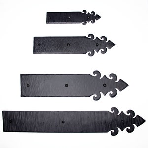 May include: Four black metal hinges with decorative scrollwork. The hinges are arranged in order of size, with the largest hinge at the bottom and the smallest hinge at the top.
