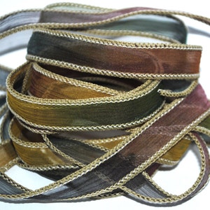Op de afbeelding: Een spoel met bruin, groen en gouden lint met een gouden rand. Het lint is doorschijnend en heeft een subtiele glans.