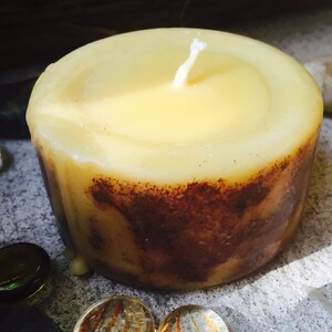 May include: A yellow beeswax candle with a white wick. The candle has a brown, textured base.
